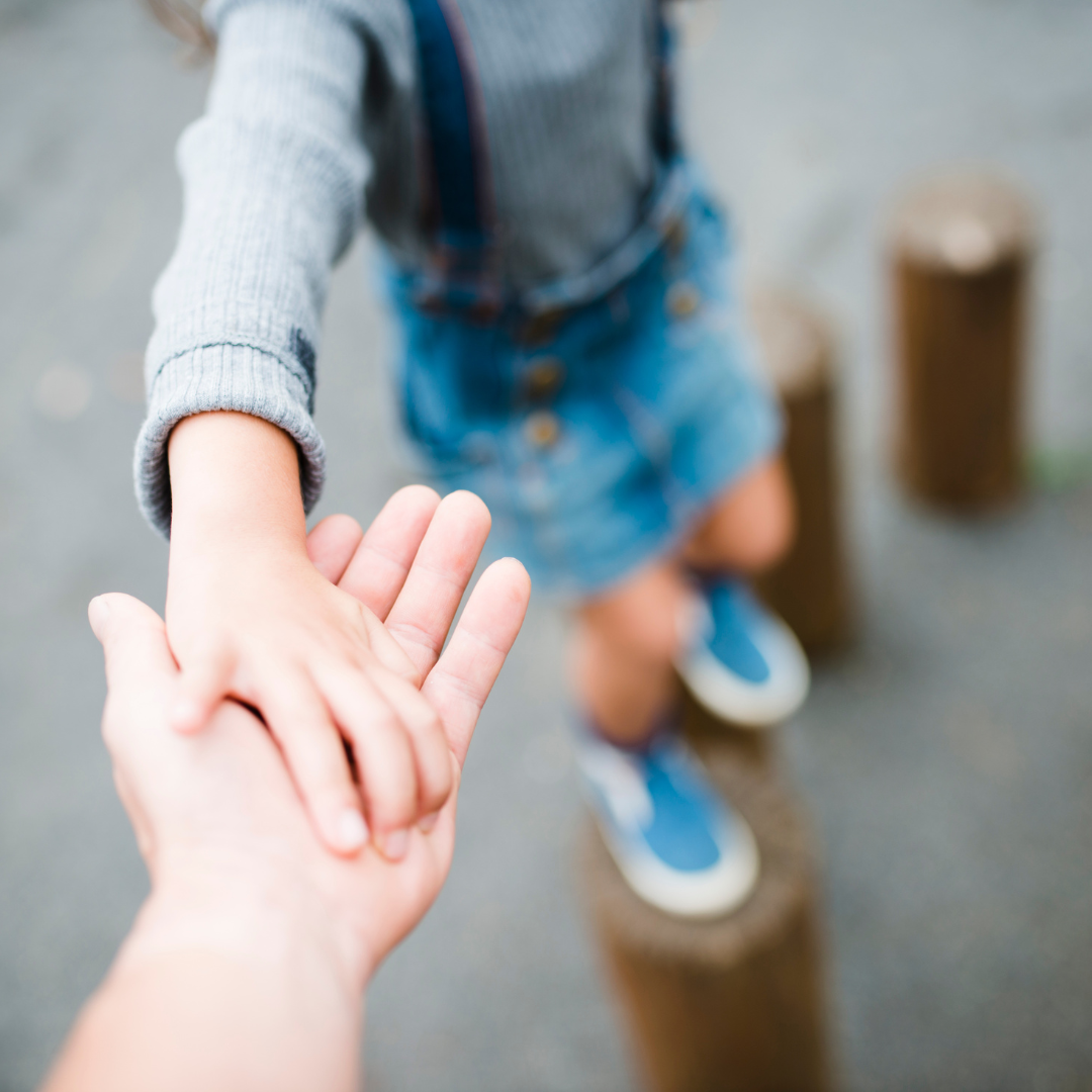 Une main d'adulte prend celle d'un enfant en équilibre sur un jeu de poteaux. Apprendre à donner des consignes claires et sans s'énerver en restant positif et respectueux à l'enfant lui permettra de mieux assimiler les r^gles au quotidien.